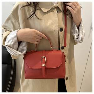 Detail of red pebbled leather crossbody bag with gold buckle on beige trench coat