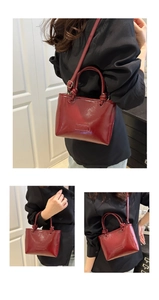 Detail of dark red glossy patent leather tote with stylish knot handles and shoulder strap