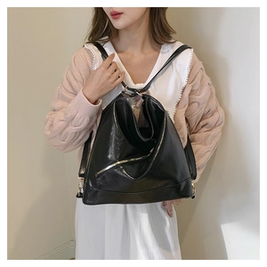 Detail of glossy black leather backpack featuring silver diagonal zippers and folded design