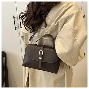 Detail of lychee textured dark brown leather handbag with gold metal buckle on beige coat