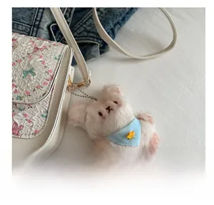 Close-up of cute plush animal charm with blue scarf hanging on floral patterned bag