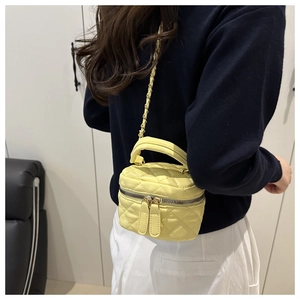 Detailed view of yellow quilted mini handbag with gold chain strap on blue sweater