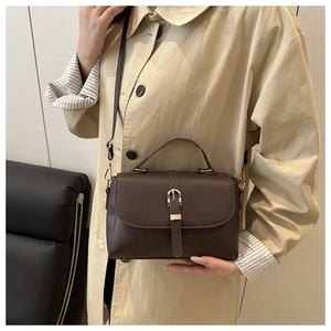 Detail of deep brown lychee texture handbag with gold buckle worn with a beige trench coat