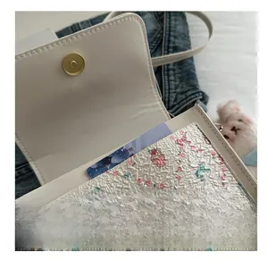 Close-up of white leather handbag featuring printed inner lining and gold magnetic buckle