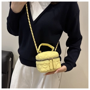 Macro detail of yellow quilted leather camera bag with gold chain strap and dual zippers