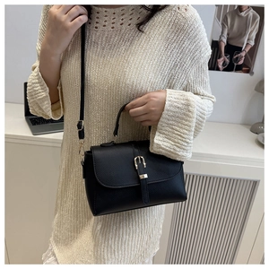 Detail of black pebbled leather handbag with gold buckle closure and top handle strap