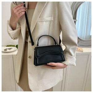 Detail of black rectangular crossbody bag with wave flap design and gold hardware