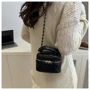 Detail of a black quilted mini chain bag worn as a crossbody on a stylish knitted sweater
