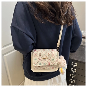 Detail view of a white crossbody bag with floral patterns and a plush rabbit charm