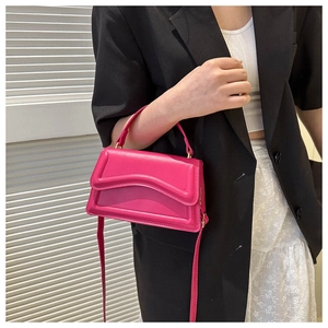 Detail of rose pink crossbody bag with wavy stitching worn over a black blazer