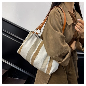 Detail of striped canvas tote bag with leather straps and gold metal ring connectors
