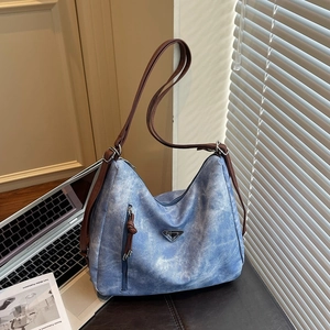 Large denim tote bag with brown leather straps and metal logo in a lifestyle setting
