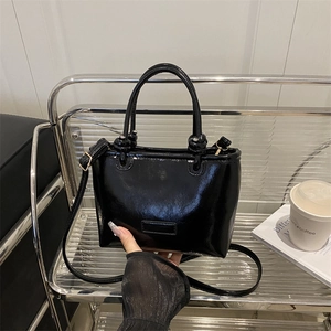 Chic black patent leather square handbag with knotted handles and adjustable shoulder strap