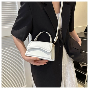 Detailed view of white minimalist handbag featuring wavy flap design and gold hardware
