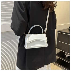 White PU leather handbag with unique wavy flap and gold hardware worn over shoulder
