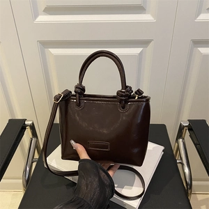 Deep brown glossy patent leather crossbody bag with creative knotted handle design