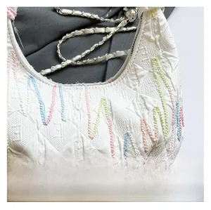 Detailed close-up of colorful wavy embroidery and embossed texture on a white chain bag