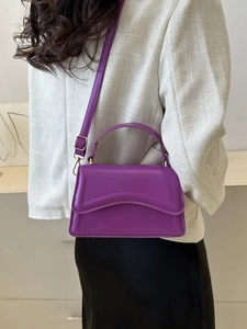 Detail of purple matte leather handbag with gold metal hardware and flap closure design