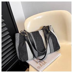 Close-up of striped canvas tote bag featuring black leather straps and gold hardware