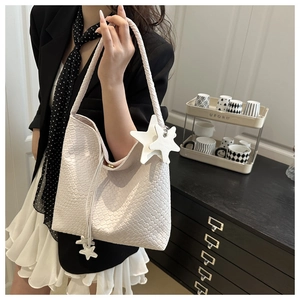 Detail of cream woven tote bag with star pendant shown on a model in a modern room