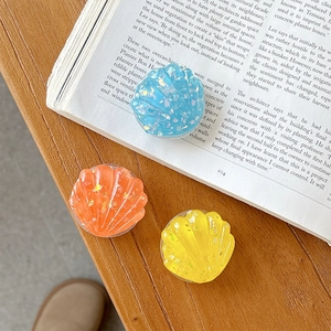 Close-up of shell-shaped resin phone grips in blue, orange, and yellow with gold foil