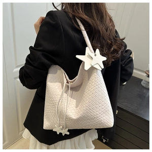 Detail of white woven hobo bag with two star pendants and a braided shoulder strap