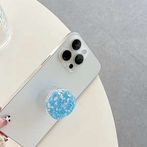 Blue shell-shaped phone grip with iridescent foil flakes on a white smartphone back