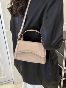 Detail view of beige crossbody bag with wavy lid and gold hardware on a model