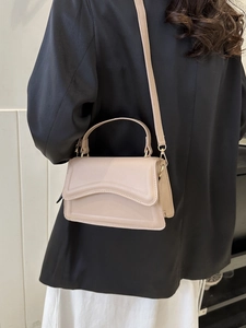 Detail of nude minimalist handbag featuring unique wavy edge and bright gold hardware