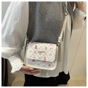 Detail of white crossbody bag featuring colorful bear and floral prints with gold logo