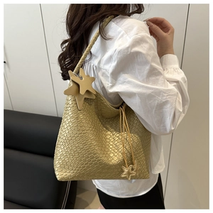 Detail of champagne gold woven tote bag with star charms worn by a model in a white shirt