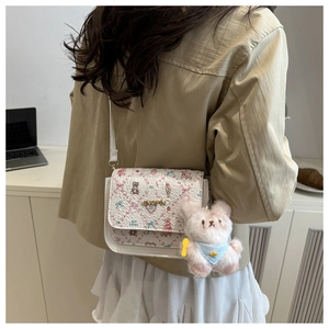 Détail d'un sac bandoulière blanc avec imprimé fleuri et ourson et breloque peluche