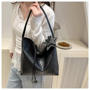 Detail of black woven shoulder bag with star charm worn by a model in a cozy setting