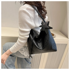Detail view of black woven tote bag with star charms on a model in a minimalist room