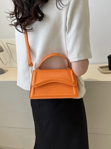 Detail of a bright orange crossbody bag with wavy embossed lines on a black dress