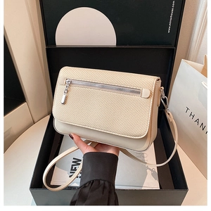 Detail of cream-colored flap crossbody bag with fabric texture and metal zipper detail