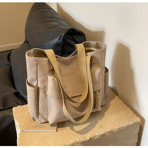 Detail of beige canvas tote bag with front pocket and side compartments on stone pedestal