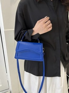 Close-up of blue structured handbag with top handle and adjustable shoulder strap on model