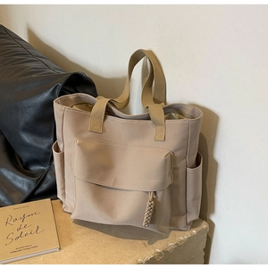 Detail of beige canvas tote bag with front flap pocket on a textured stone surface