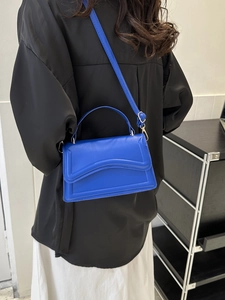Blue crossbody bag with chic pleated fold detail shown from a side view on a model