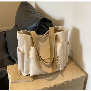 Close-up of the beige canvas tote bag showing front pockets and khaki webbing straps