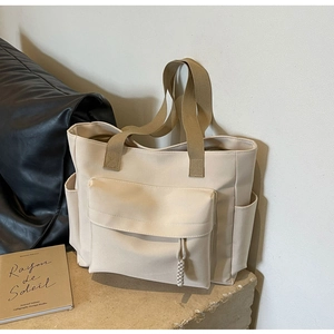 Detailed macro view of cream canvas tote bag showing the front flap pocket and side pocket