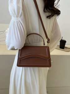 Brown faux leather crossbody bag with wavy flap detail shown on a white dress