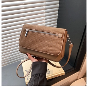 Detail of a brown crossbody bag with woven texture and a decorative front metal zipper