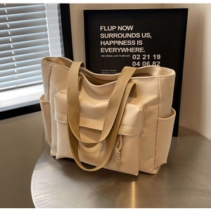 Detail of a beige canvas tote bag showing functional side pockets and wide strap