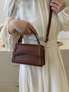 Close-up of a dark brown crossbody bag featuring elegant curved flap and gold hardware