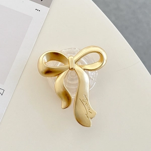 Detail of matte gold bow phone stand with artistic engraving on minimalist background