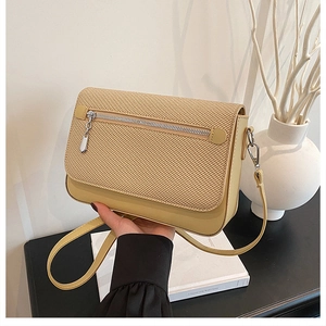 Detail of beige crossbody bag with woven texture flap and metallic zipper hardware