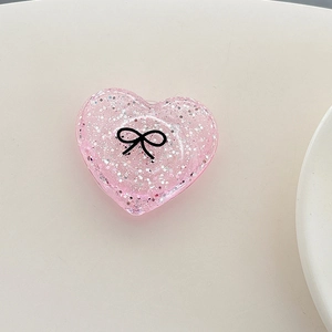 Detail of pink glitter heart phone socket with a minimalist black bow on a beige surface