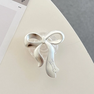 Detail view of a matte silver bow-shaped phone grip with Denise engraving on a desk